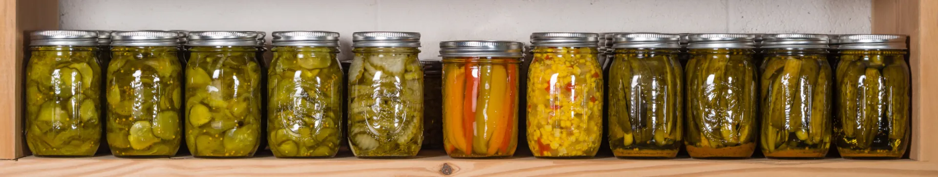 row of jars on a shelf containing various preserved vegetables